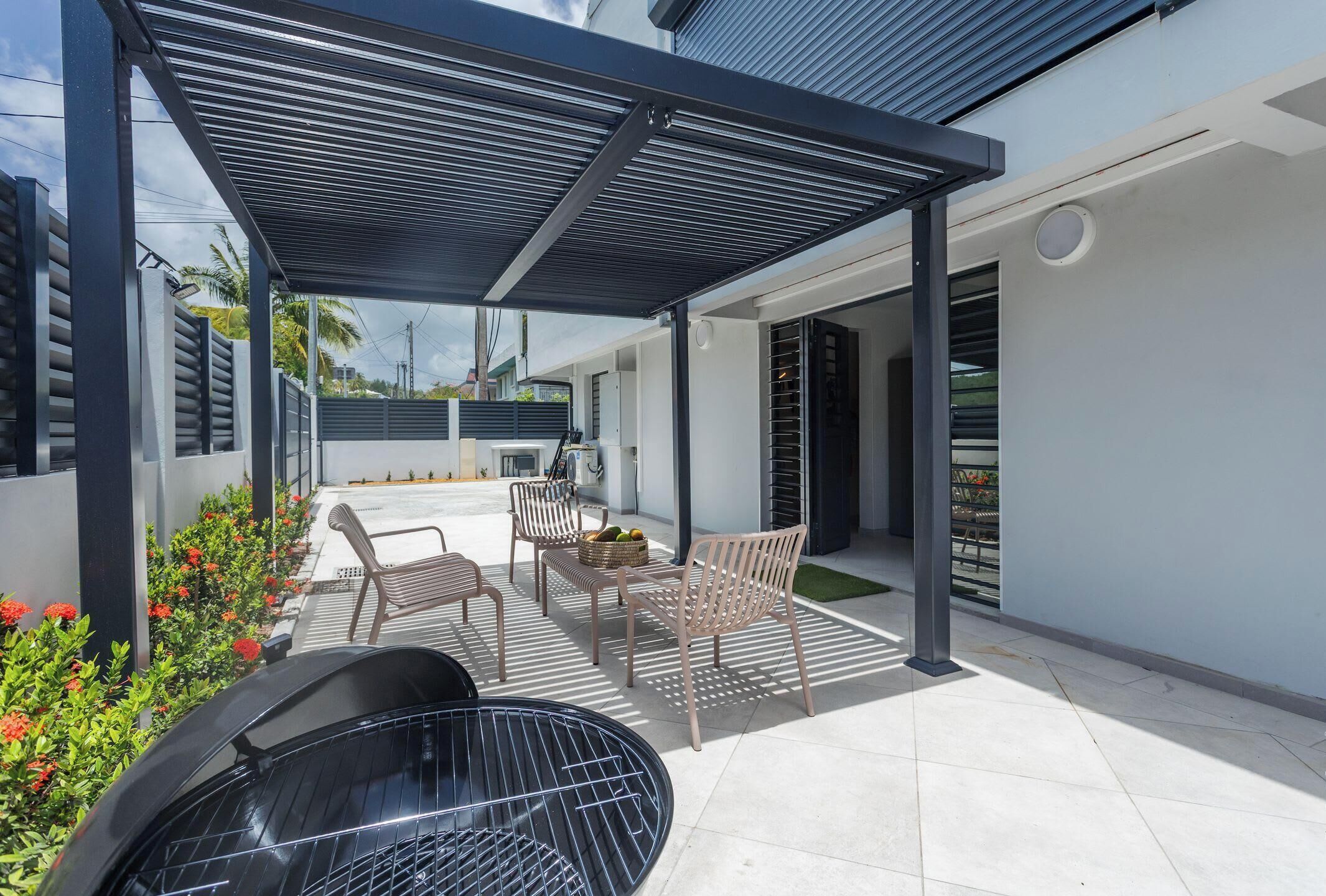 Une terrasse extérieure couverte, équipée d’un barbecue, de sièges et offrant une vue sur la rue.