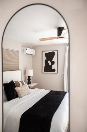 A bedroom with a bed, bedside table, lamp, air conditioning unit, and a framed artwork on the wall. - The Nile (Fort Myers Beach)