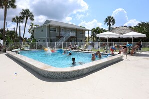 A swimming pool with a tiled edge, surrounded by a white fence, palm trees, and a building with a balcony. - The Nile (Fort Myers Beach)
