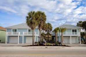 A two-story residential building with a flat roof, a balcony on the second floor, and a front yard with palm trees. - The Nile (Fort Myers Beach)