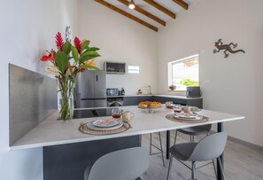 A modern kitchen with a central island, a dining area with two chairs, and a decorative wall piece. - La Villa de Solange - Canopée (La Trinité)
