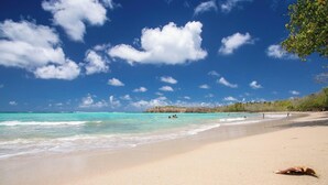 Une plage à l’eau turquoise et limpide, avec un rivage sablonneux et quelques personnes qui se baignent.