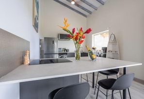 A modern kitchen with a central island, a dining area with chairs, and a surfboard shelf. - La Villa de Solange - Azur (La Trinité)