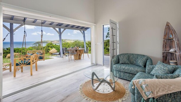 A spacious room with a large glass door leading to an outdoor area with a view of the ocean. - La Villa de Solange - Azur (La Trinité)
