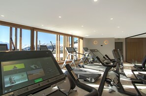 A modern gym with treadmills, exercise bikes, and a large screen displaying workout routines. - T2 au pied des pistes | Piscine sur place | Garage (Alpe d'Huez)