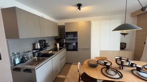 Una cocina moderna con electrodomésticos integrados, una zona de comedor con una mesa redonda e iluminación colgante.