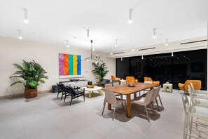 Ein moderner Konferenzraum mit Holztisch, weißen Stühlen und einem farbenfrohen abstrakten Gemälde an der Wand.