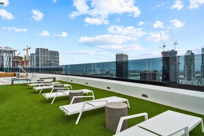Eine Dachterrasse mit weißen Lounge-Sesseln und einer Glasbrüstung mit Blick auf eine Skyline, die moderne Gebäude und Baukräne zeigt.