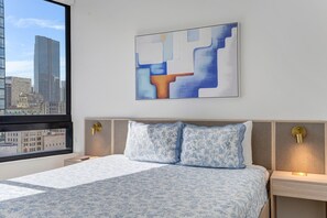 Ein Hotelzimmer mit Bett, Blick auf die Stadt und einem modernen, abstrakten Gemälde an der Wand.