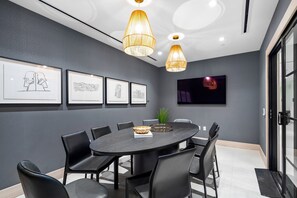 Ein Konferenzraum mit rundem Tisch, schwarzen Stühlen, gerahmten Bildern an der Wand und Pendelleuchten.