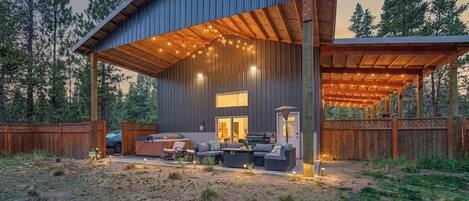 A modern outdoor patio with a covered seating area, a barbecue grill, and a view of the surrounding forest.