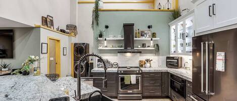 A modern kitchen with a central island, stainless steel appliances, and a wooden ceiling.