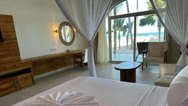 Quarto de hotel com uma cama, escrivaninha, cadeira e vista para a praia.