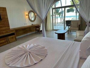 A hotel room with a bed, a desk, a chair, and a view of the beach. - Royal Mandarin Hotel & Resort (Kiwengwa)