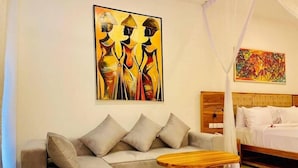 Quarto moderno com cama, sofá, mesa de centro de madeira e duas pinturas na parede.