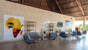 Amplo espaço interno com teto alto e um grande mural de uma paisagem africana. Vários espaços de estar com móveis modernos e vitrines de vidro.
