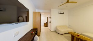 A modern living room with a flat-screen TV, wooden furniture, a ceiling fan, and a wall-mounted air conditioner. - Royal Mandarin Hotel & Resort (Kiwengwa)
