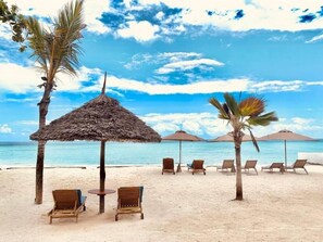 A beach with thatched umbrellas, lounge chairs, and palm trees. - Royal Mandarin Hotel & Resort (Kiwengwa)