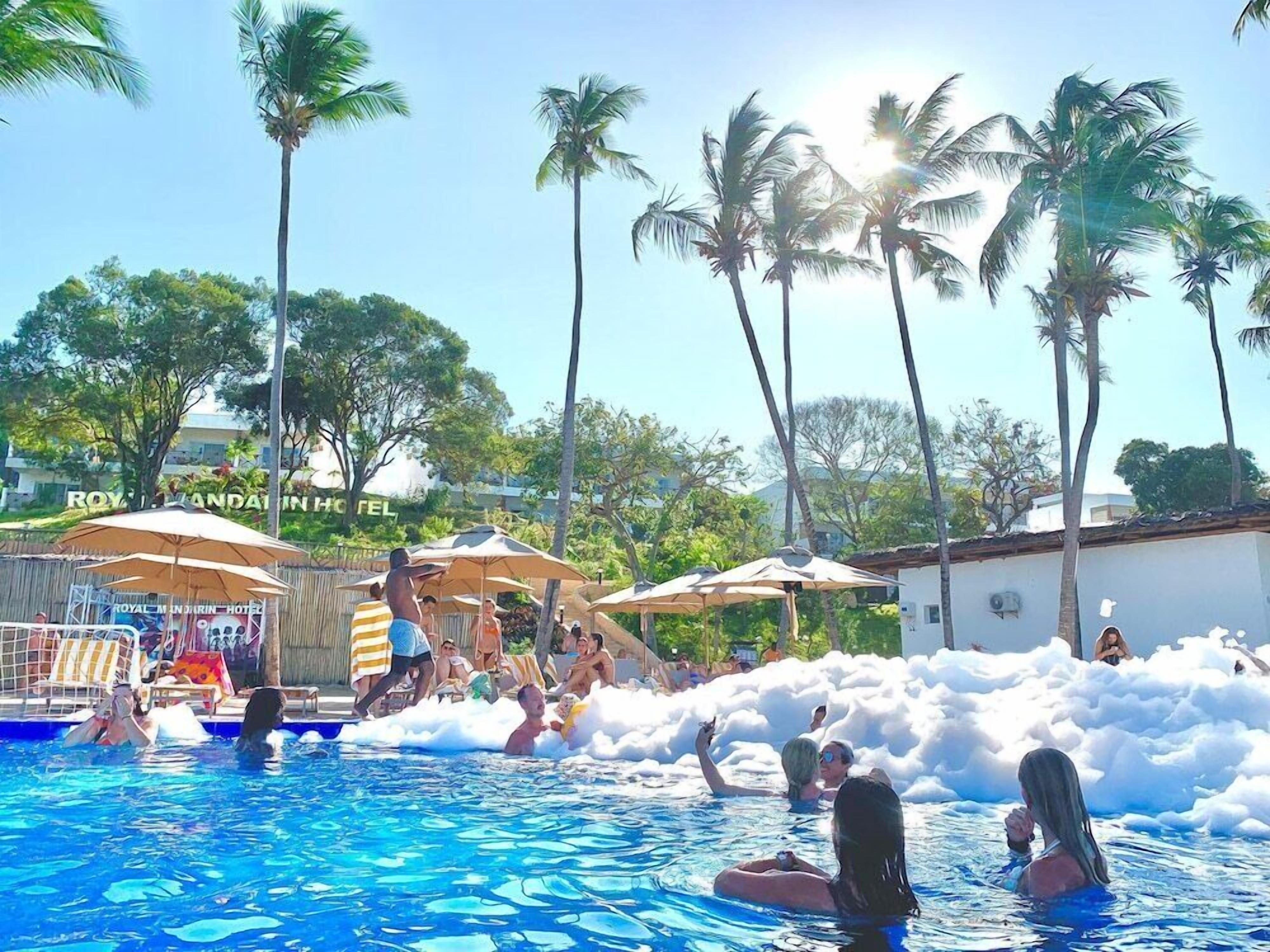 Uma área de piscina com palmeiras, guarda-sóis e uma placa do Hotel Royal Caribbean.