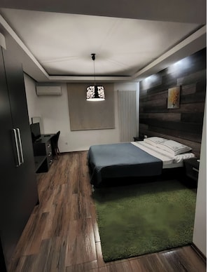 Een slaapkamer met een bed, bureau, stoel, kledingkast, radiator en hanglamp.