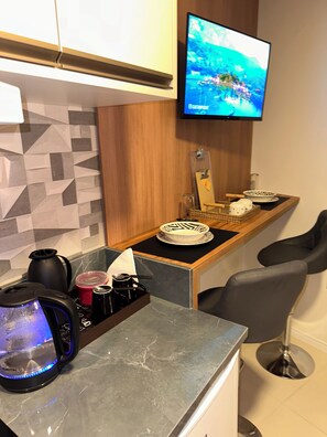 A modern kitchen with a flat-screen TV mounted above the counter, a coffee maker, a kettle, and a bowl set on the counter. - Fully furnished loft 210 in the Fazenda neighborhood. (Itajaí)