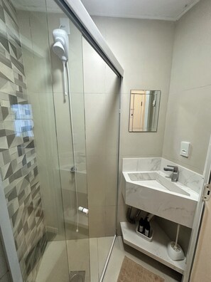 A modern bathroom with a glass-enclosed shower, a marble sink, and a mirror. - Fully furnished loft 210 in the Fazenda neighborhood. (Itajaí)