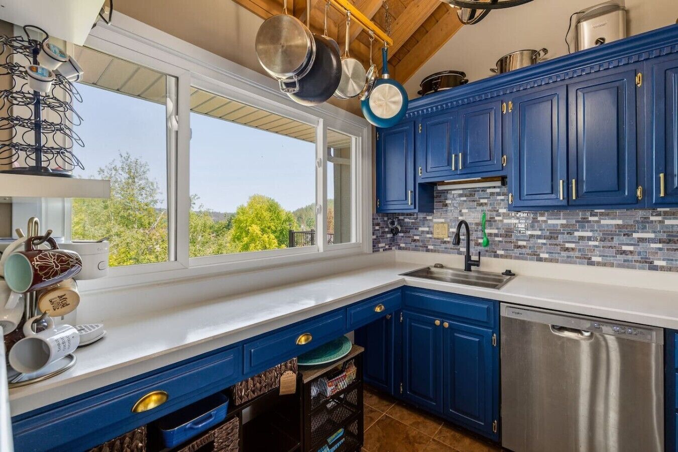 A kitchen with blue cabinets, a stainless steel dishwasher, and hanging pots.