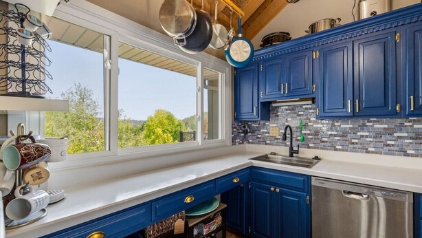 A kitchen with blue cabinets, a stainless steel dishwasher, and hanging pots. - Black Hills Townhome -Community Pool-Near Downtown (Rapid City)