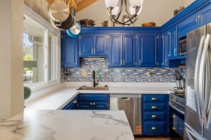 Una cocina con armarios azules, encimera de mármol, refrigerador de acero inoxidable y salpicadero de azulejos.