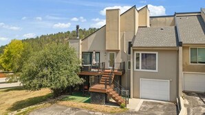 A residential building with a garage, a staircase leading to a balcony, and a tree in the yard. - Black Hills Townhome -Community Pool-Near Downtown (Rapid City)