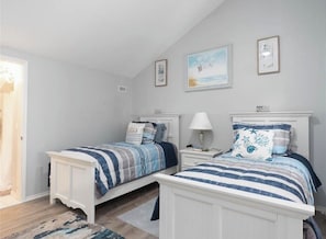 Un dormitorio con dos camas, una mesita de noche con lámpara y una puerta que da a otra habitación.