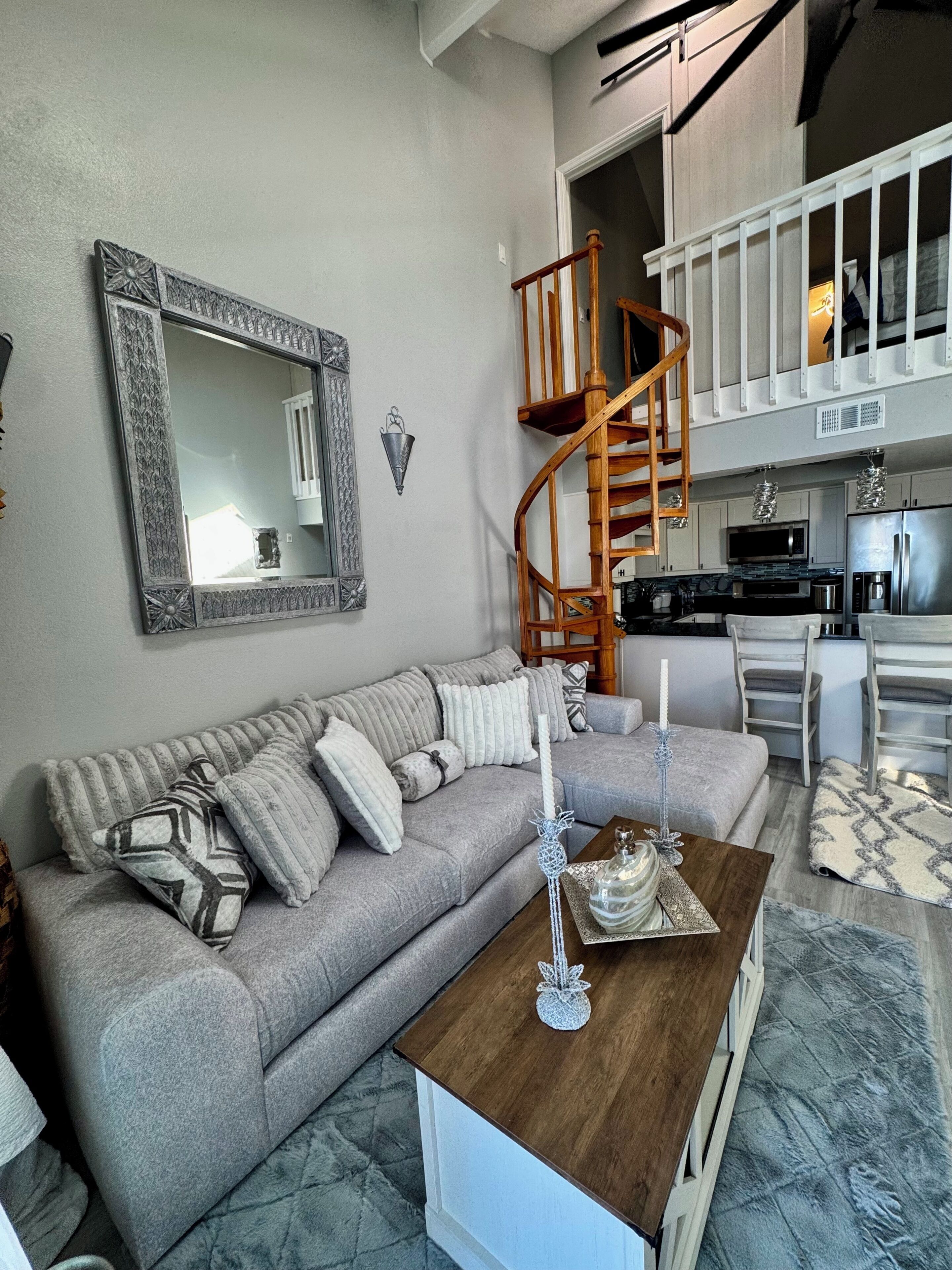 A living room with a grey sofa, a wooden coffee table, and a spiral staircase leading to an upper level.