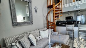 Un salon avec un canapé gris, une table basse en bois et un escalier en colimaçon menant à un niveau supérieur.