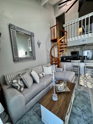 A living room with a grey sofa, a wooden coffee table, and a spiral staircase leading to an upper level. - Superb 2-bedroom condo with large pool in wonderful Port Charlotte (Port Charlotte)