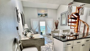Une cuisine compacte avec un coin repas, des meubles blancs, un banc en bois et une vue à travers une porte vitrée.