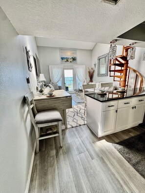 A compact kitchen with a dining area, white cabinetry, a wooden bench, and a view through a glass door. - Superb 2-bedroom condo with large pool in wonderful Port Charlotte (Port Charlotte)