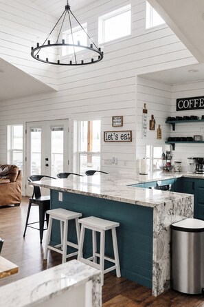 A modern kitchen with a marble island, bar stools, a coffee station, and a sign that says 'let's eat'. - Casa Blanca Old Town Estate + Vineyard View + Pool (Cottonwood)