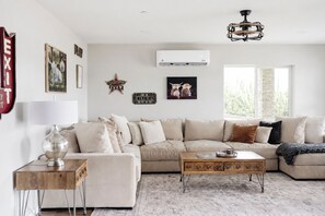 Un salon comprenant un canapé d’angle, une table basse, une lampe et des éléments de décoration murale, notamment un panneau indiquant qu’il s’agit d’une salle de cinéma et un panneau d’accueil.