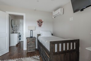 A bedroom with a wooden bed, a bedside table, a lamp, a wall-mounted air conditioner, and a mirror. - Casa Blanca Old Town Estate + Vineyard View + Pool (Cottonwood)