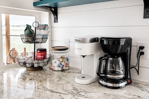 Et køkken med kaffemaskine, en beholder med kaffekapsler og en kurv med køkkenredskaber.