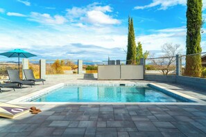 A swimming pool with lounge chairs and a sun umbrella, surrounded by a fence and tall trees. - Casa Blanca Old Town w/ Pool & Red Rock Views (Cottonwood)