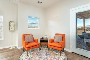 A room with two orange armchairs, a small table with a book and a cup, a colorful rug, a clock on the wall, and a view through a glass door. - Casa Blanca Old Town w/ Pool & Red Rock Views (Cottonwood)