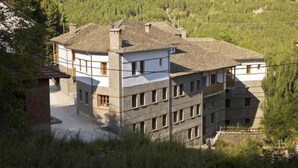 Un edificio de varios pisos con fachada de piedra, múltiples balcones y un paisaje natural circundante.