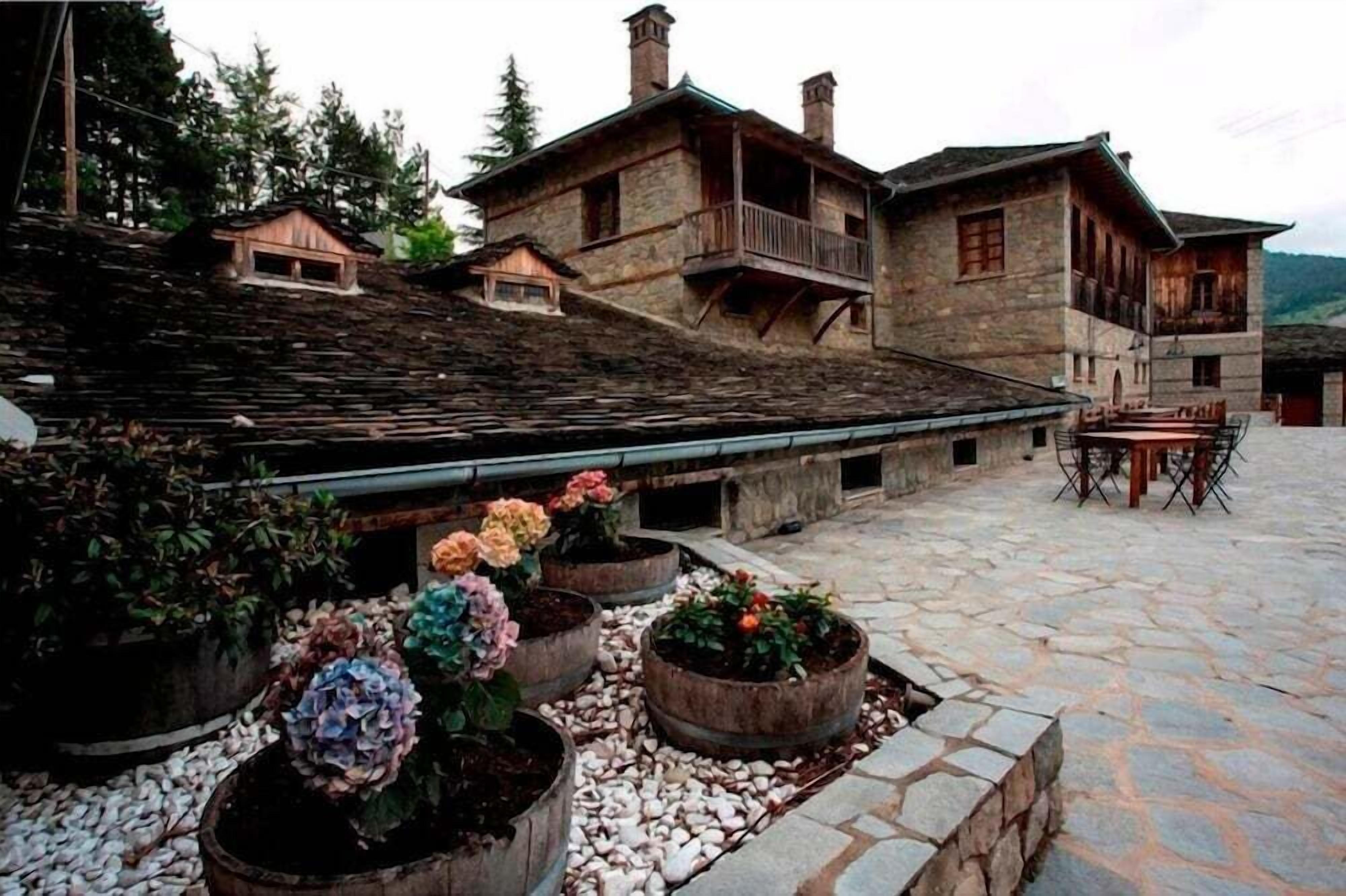 A stone courtyard with rustic buildings, outdoor seating, and flower planters.