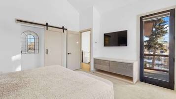 A bedroom with a bed, a sliding door, a TV mounted on the wall, and a view through a door to the outside.