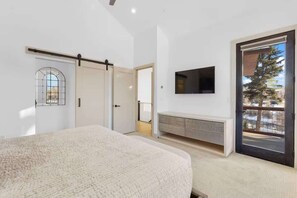 A bedroom with a bed, a sliding door, a TV mounted on the wall, and a view through a door to the outside. - NEW! The Vista On The Blue - Downtown Riverfront (Silverthorne)