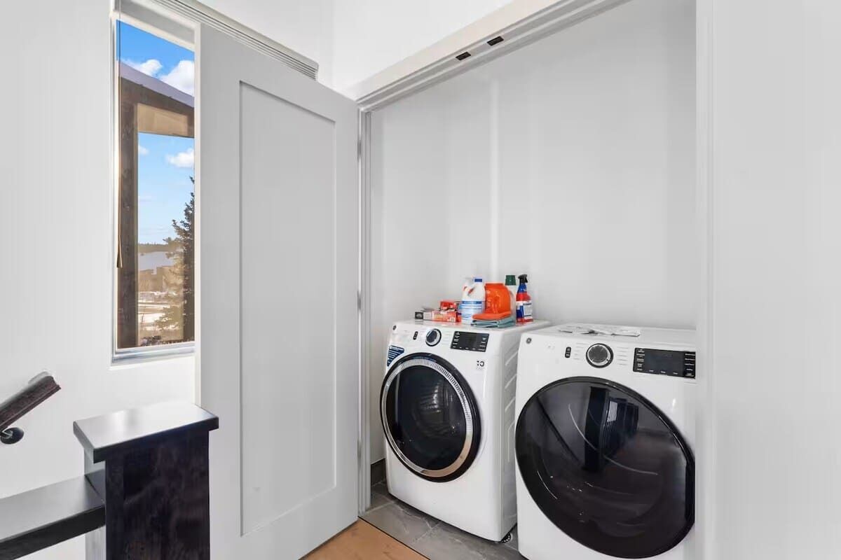 A laundry room with two washing machines, a small table, and a window with a view of the outside.