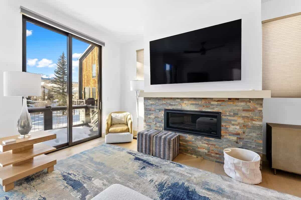 A modern living room with a large TV, fireplace, and a view of a mountain.