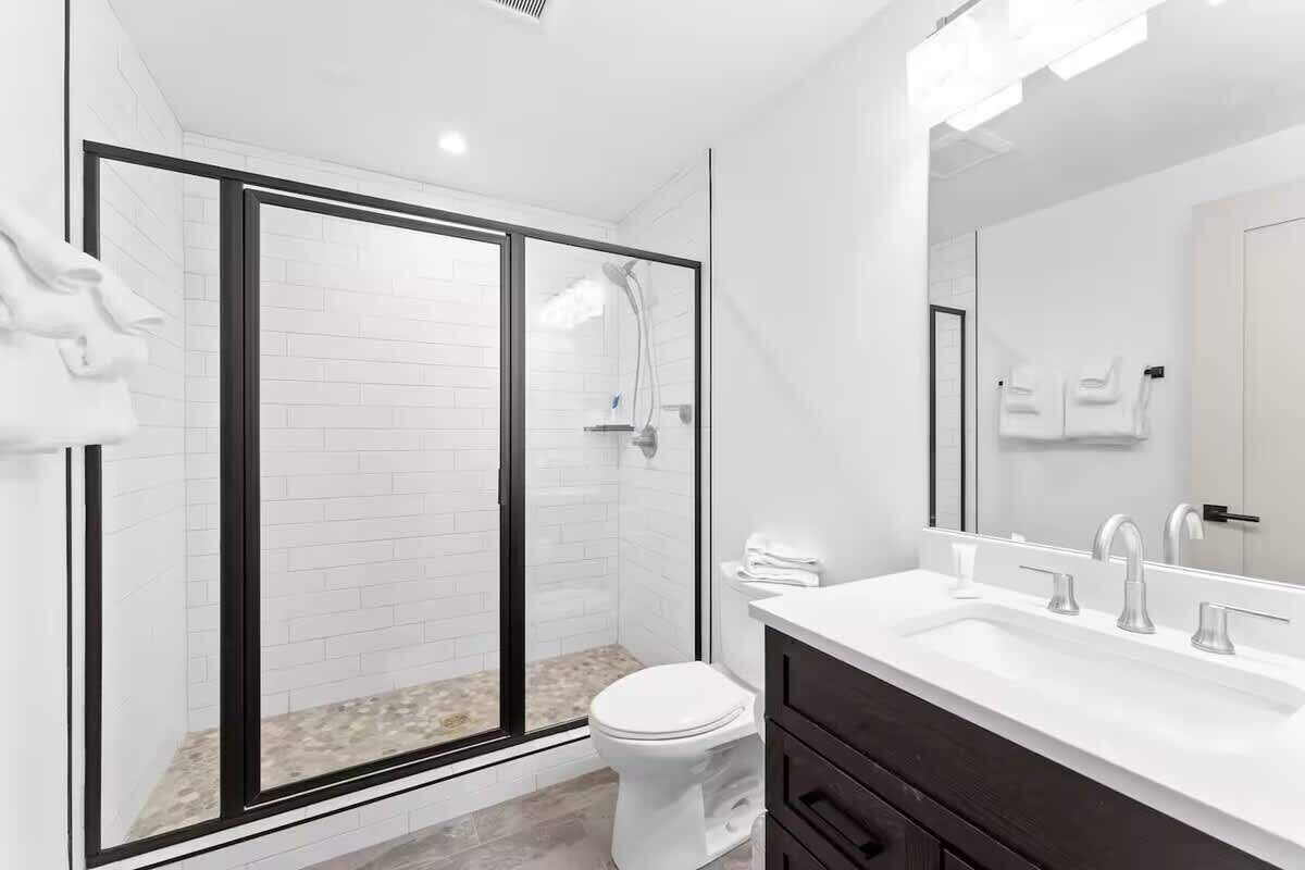 A modern bathroom with a glass-enclosed shower, a white toilet, and a vanity with a mirror.