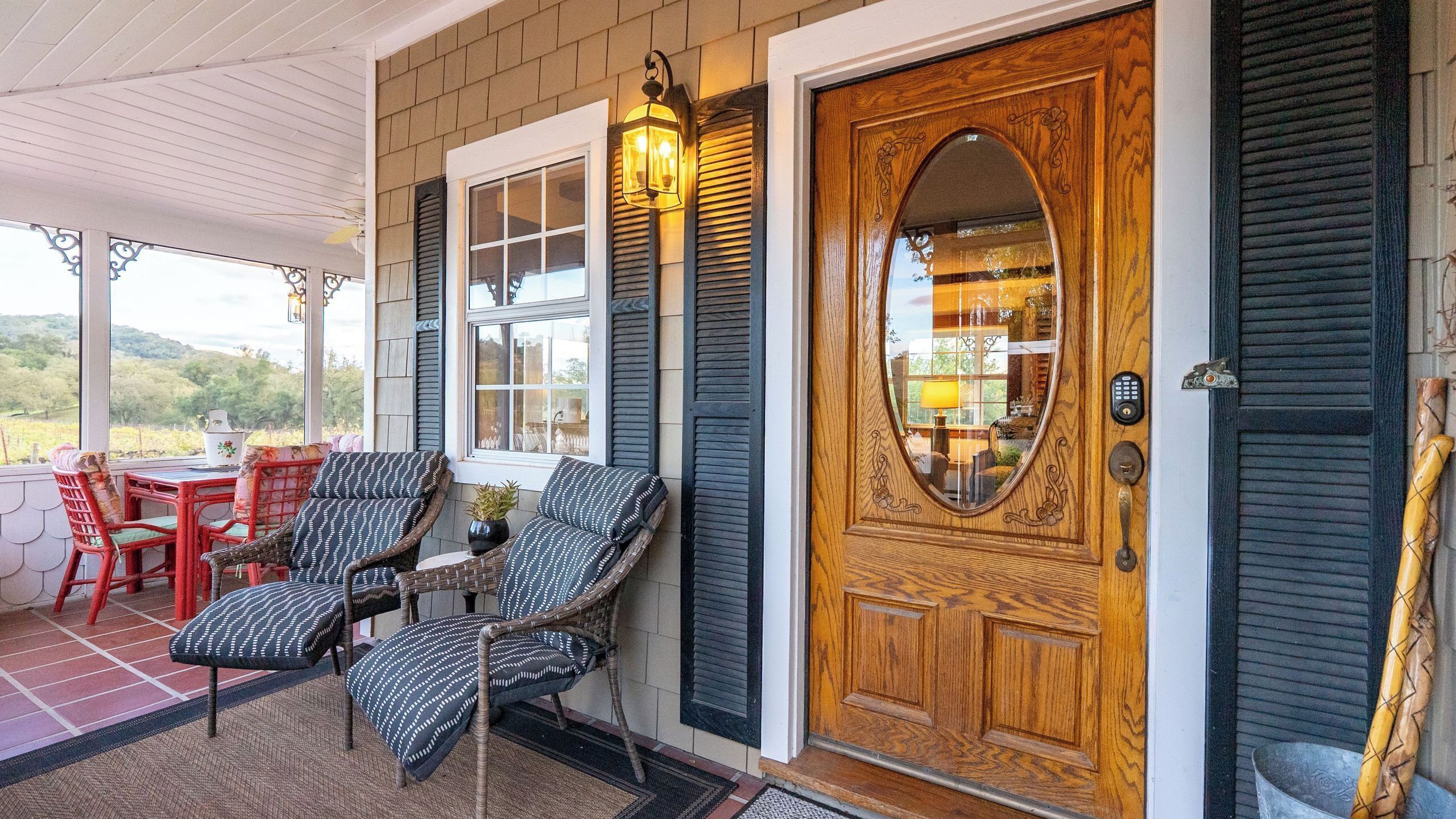 A porch with wicker furniture, a wooden door with a glass panel, and a lantern.